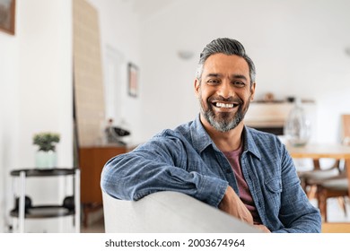 Portrait Of Handsome Mature Man Relaxing On Couch At Home While Looking At Camera. Mixed Race Man In Casual Clothing Sitting On Sofa And Smiling With Copy Space. Successful Happy Middle Eastern Guy.