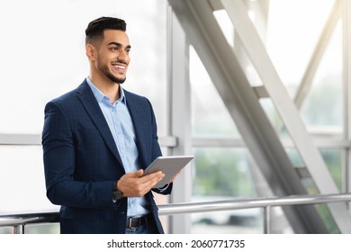 Portrait Of Handsome Middle Eastern Businessman Using Digital Tablet While Waiting For Flight At Airport Terminal, Smiling Arab Man In Suit Holding Tab Computer And Looking Away, Copy Space