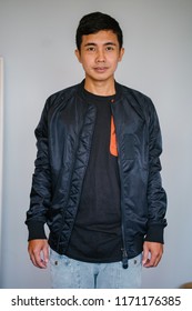 Portrait of a handsome middle-aged Malay Singaporean man in a studio. He is taking his head shot against a white backdrop in a studio. The man is wearing a sporty black jacket and has short hair. 