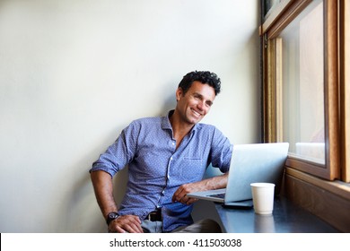 Portrait Of A Handsome Modern Man Smiling With Laptop At Cafe