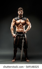 Portrait of handsome muscular gladiator with sword. Studio shot. Black background.
