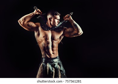 Portrait of handsome muscular gladiator with two swords. Studio shot. Black background.