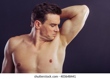 Portrait Of Handsome Naked Man Smelling His Underarm, On A Dark Background