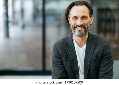Portrait of a handsome office worker or ceo. Confident stylish bearded middle aged caucasian man in formal jacket and white t-shirt smiles and looks directly into the camera - Shutterstock ID 1938107200