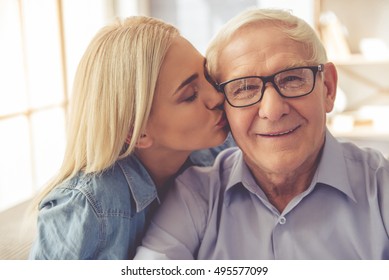 Portrait of handsome old man and beautiful young girl. Girl is kissing her parent in cheek, he is looking at camera and smiling