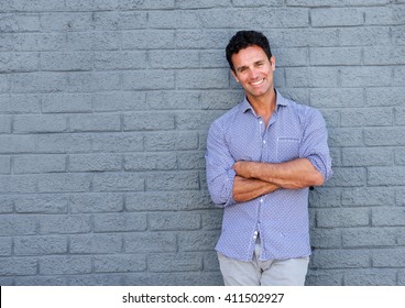 Portrait Of A Handsome Older Man Smiling With Arms Crossed Against Gray Background