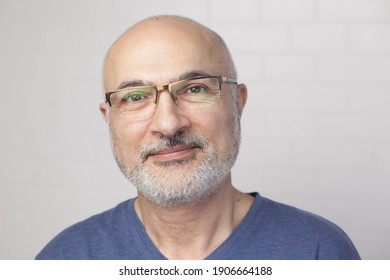 Portrait of a handsome positive 50 years old man with glasses, unshaven hair in a blue t-shirt indoors.