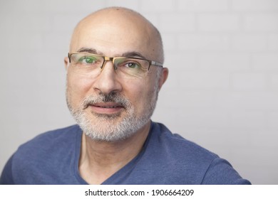 Portrait Of A Handsome Positive 50 Years Old Man With Glasses, Unshaven Hair In A Blue T-shirt Indoors.