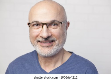 Portrait of a handsome positive 50 years old man with glasses, unshaven hair in a blue t-shirt indoors.