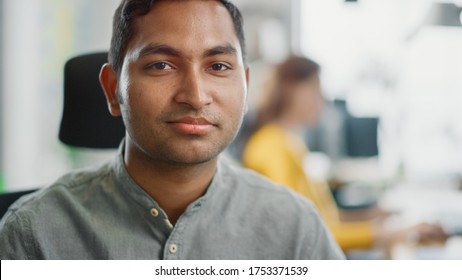 Portrait Of Handsome Professional Indian Man At His Working Desk, Looking At The Camera. Successful Man Working In Bright Diverse Office.