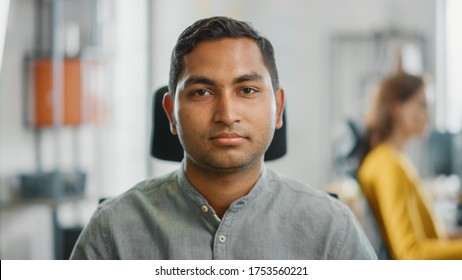 Portrait Of Handsome Professional Indian Man At His Working Desk, Looking At The Camera. Successful Man Working In Bright Diverse Office.