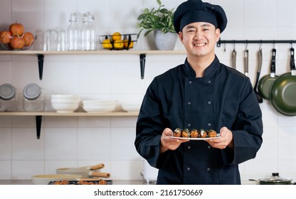 Portrait Handsome Professional Japanese Male Chef Wearing Black Uniform, Hat, Cooking, Showing Takoyaki Street Food, Smiling With Confidence, Happiness, Standing In Kitchen. Restaurant, Hotel Concept