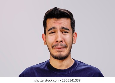 a portrait of a handsome sad Asian man looking at camera , being annoyed and upset , disturbed and unhappy  feeling bad , negative emotions  about to cry , in navy blue t shirt on gray background  - Shutterstock ID 2305141339