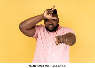 Portrait Of Handsome Sad Frustrated Man Wearing Pink Shirt Showing Looser Gesture And Pointing At Camera, Looking With Grumpy Face. Indoor Studio Shot Isolated On Yellow Background.