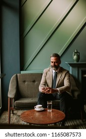 Portrait of handsome senior businessman drinking coffee and using mobile phone in lobby - Shutterstock ID 1165087573