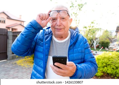 Portrait Of Handsome Senior Man 70-75 Years Old Using Smartphone Outdoors. Older Man Read Sms With Phone. Lifestyle, Technology Concept. Happy Grandfather