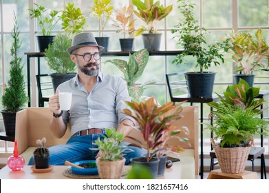 Portrait of handsome senior man is happily taking care of the plants in the nursery and drinking coffee . Living a happy retirement life at home concept - Powered by Shutterstock