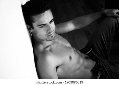 Portrait of handsome shirtless man sitting against wall with muscular body.