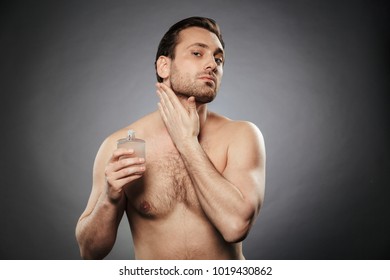 Portrait Of A Handsome Shirtless Man Using Aftershave Lotion Isolated Over Gray Background