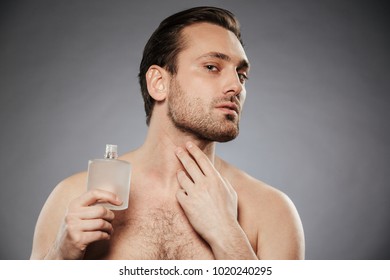 Portrait Of A Handsome Shirtless Man Using Aftershave Lotion Isolated Over Gray Background