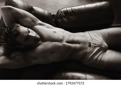 Portrait of handsome shirtless muscular man with beard and sixpack abs lying in leather armchair, sleeping.