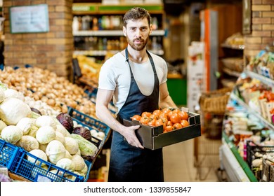 Portrait Of A Handsome Shop Worker Or Farmer Holding Box With Fresh Tomatoes In The Vegetable Department In The Supermarket