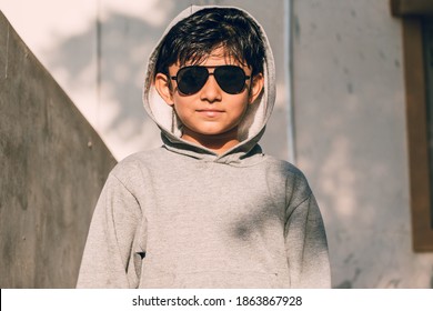 Portrait Of Handsome, Smart Indian Kid Standing Indoors, Wearing Sunglasses And Grey Color Hoodie. 