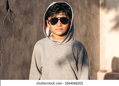 Portrait Of Handsome, Smart Indian Kid Standing Indoors, Wearing Sunglasses And Grey Color Hoodie. 