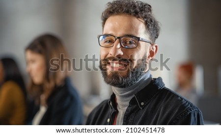 Portrait of a Handsome Smart Male Student, Studying in University, Fondly Smiling on Camera. He Wears Glasses and Has a Beard and Short Curly Hair. Works on Computer in College.