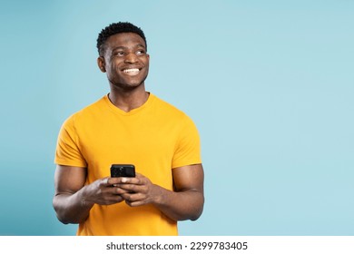 Portrait of handsome smiling African American man holding mobile phone shopping online with sale, looking away isolated on blue background. Happy hipster guy using mobile app ordering food, copy space - Powered by Shutterstock