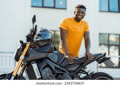 Portrait of handsome smiling african american man, biker looking at camera and posing near motorcycle at the street. Journey, freedom, transportation concept - Powered by Shutterstock