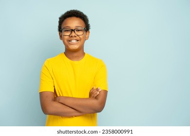 Portrait of handsome smiling African American boy in yellow casual t shirt wearing glasses with crossed arms standing isolated on blue background, copy space. Education concept - Powered by Shutterstock