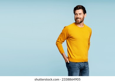 Portrait of handsome smiling bearded man wearing autumn yellow sweater, stylish jeans isolated on blue background. Portrait of successful middle aged fashion model posing for pictures, studio shot