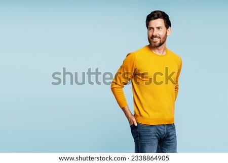 Portrait of handsome smiling bearded man wearing autumn yellow sweater, stylish jeans isolated on blue background. Portrait of successful middle aged fashion model posing for pictures, studio shot