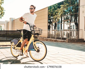 Portrait of handsome smiling stylish hipster lambersexual model.Man dressed in white T-shirt. Fashion male riding a bike on the street background in sunglasses - Powered by Shutterstock