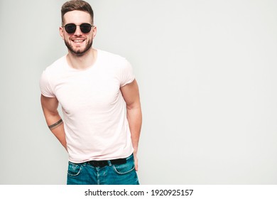 Portrait of handsome smiling stylish hipster lambersexual model.Man dressed in white T-shirt and jeans. Fashion male posing on grey background in studio in sunglasses - Powered by Shutterstock