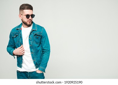 Portrait of handsome smiling stylish hipster lambersexual model.Man dressed in jacket and jeans clothes. Fashion male posing on grey background in studio in sunglasses