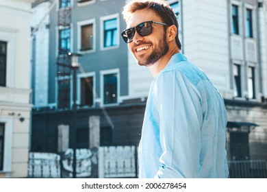 Portrait of handsome smiling stylish hipster lambersexual model.Modern man dressed in blue shirt. Fashion male posing near skyscraper on the street background in sunglasses. Outdoors at sunset  - Powered by Shutterstock