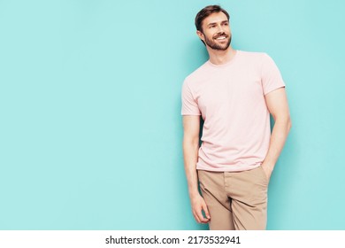 Portrait Of Handsome Smiling Stylish Hipster Lambersexual Model. Sexy Man Dressed In Pink T-shirt And Trousers. Fashion Male Isolated On Blue Wall In Studio