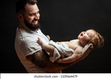 Portrait of handsome strong beared man holding on hands adorable little baby over black background with copyspace, spending time together, lovely young father. Parentship, love and happiness concept
