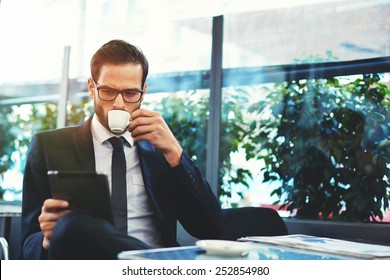 Portrait of handsome successful man drink coffee and look to the digital tablet screen sitting in coffee shop, business man having breakfast sitting on beautiful terrace with plants - Powered by Shutterstock