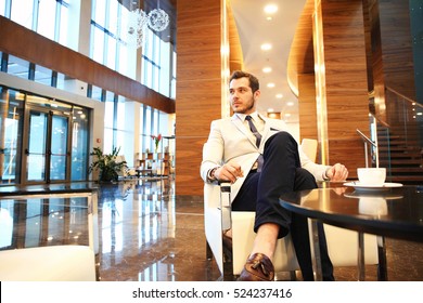 Portrait Of Handsome Successful Man Drink Coffee Sitting In Coffee Shop, Business Man Having Breakfast At Hotel Lobby