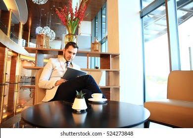 Portrait Of Handsome Successful Man Drink Coffee And Look To The Digital Tablet Screen Sitting In Coffee Shop, Business Man Having Breakfast At Hotel Lobby