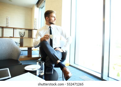 Portrait Of Handsome Successful Man Drink Coffee Sitting In Coffee Shop, Business Man Having Breakfast At Hotel Lobby