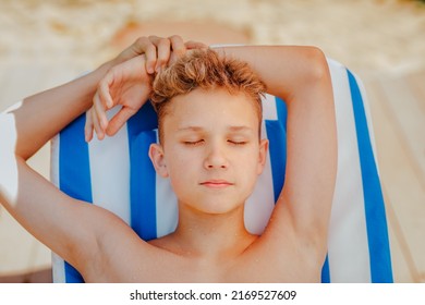 Portrait of handsome teen boy with blond wet hair relaxing on stripped beach chair with closed eyes.
