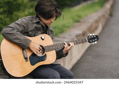 Portrait of handsome teenage boy playing guitar outdoor. Boy using classic guitar. Male alone making music - Powered by Shutterstock