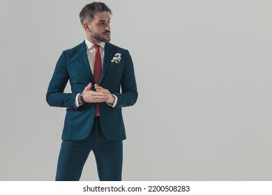 Portrait Of Handsome Unshaved Man In Elegant Suit With Tie Looking To Ide And Rubbing Palms, Applauding And Posing On Grey Background