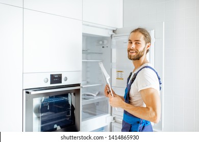 Portrait Of A Handsome Workman Installing New Refrigerator In The Modern Kitchen At Home