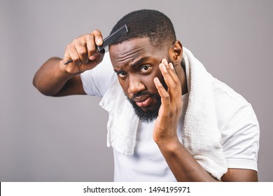 Portrait of handsome young african american black man combing his hair in bathroom. Isolated over grey background. 