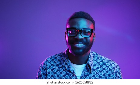 Portrait of handsome young African American male dressed in flowered shirt looking at camera and smilings and confident expression on his face in neon lights. People and lifestyle concept. Male studio